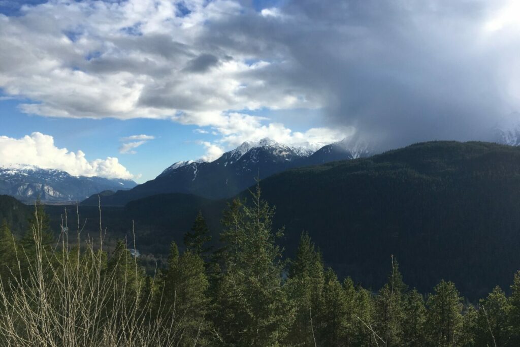 On a bright blue day in Squamish, clouds begin to cover Tsewílx̱, The Tantalus Mountain Range. Picture captured in 2017.